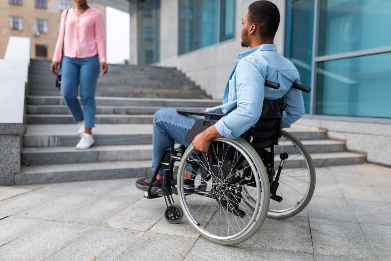 Black man in a wheelchair wearing a blue shirt looking at a set of stairs
