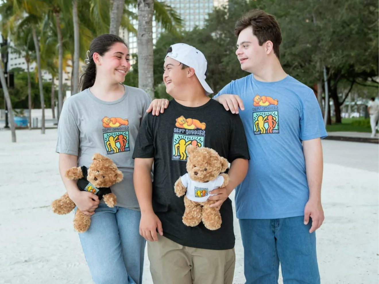 Three Best buddies program participants walking in an environment with palm trees and expressing friendship